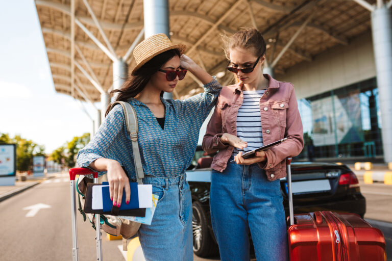 Young female friends in sunglasses holding passport with tickets